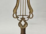une harpe ancienne en laiton posée sur un support, sur fond blanc
