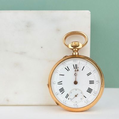 une montre de poche en or avec des chiffres romains, posée sur un bloc de marbre