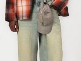 man in plaid shirt and jeans holding a purse and standing in front of a white background