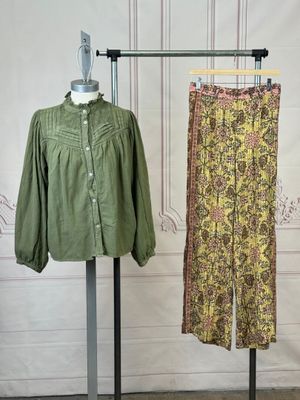 two pants and a shirt on a stand in front of a wall