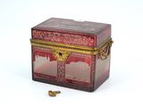 une boîte rouge avec un couvercle doré et une perle dorée au fond