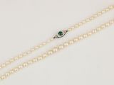 un collier de perles blanches muni d'un fermoir en émeraude et diamants