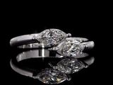 two diamond engagement rings on a reflective surface with a black background