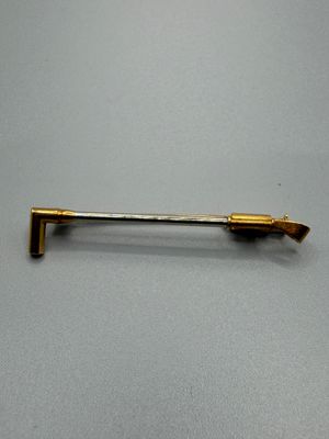 une épingle en métal plaqué or dotée d'un long manche, posée sur une surface grise