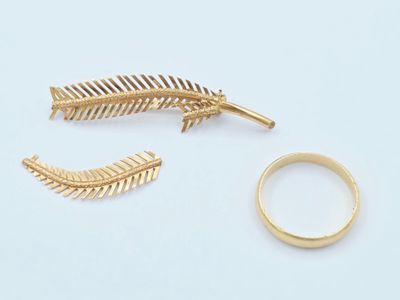 deux bagues en or et une broche en or en forme de plume, posées sur un fond blanc