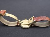 bracelet en cuir doré et rouge avec un fermoir métallique sur fond noir