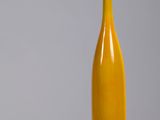 un vase jaune posé sur une table en bois, près d'un mur gris