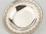 une assiette ancienne en argent posée sur un fond blanc, sur laquelle repose une plume noire
