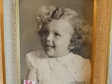 une vieille photo d'une petite fille en robe blanche, dans un cadre doré