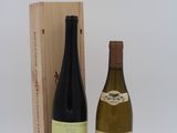 deux bouteilles de vin posées à côté d'une caisse en bois sur une surface blanche