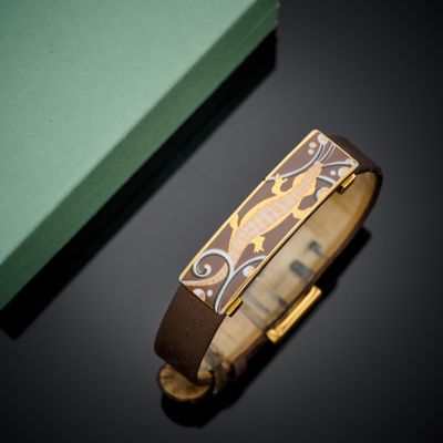 bracelet en cuir orné d'un motif doré et marron, à côté d'une boîte verte