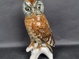 a ceramic owl sitting on a branch on a gray background