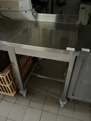 une grande table en inox dans une cuisine, avec des paniers posés par terre