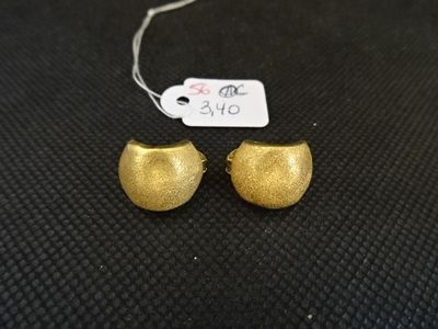 une paire de boucles d'oreilles en or posées sur une surface noire, avec une étiquette de prix