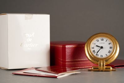 une horloge dorée posée à côté d'une boîte rouge et d'une boîte blanche
