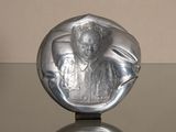 une sculpture en argent représentant une femme assise sur une table en verre