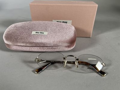 une paire de lunettes dans un étui rose, posée sur une surface grise avec sa boîte