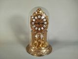 une horloge en or posée sur une table, sous un dôme en verre