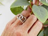 a woman ' s hand holding a silver ring with a flower in the background