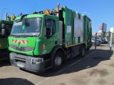 two green garbage trucks parked next to each other in a parking lot