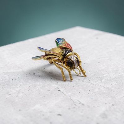 broche en forme d'abeille plaquée or, aux ailes multicolores sur fond blanc