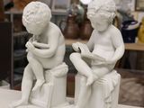 two statues of a boy and a girl sitting on a stool