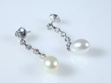 une paire de boucles d'oreilles en perles et diamants posées sur un fond blanc