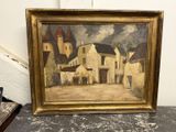 une peinture à l'huile représentant une scène de village, dans un cadre doré, posée sur une table