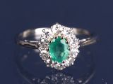 une bague ovale sertie d'une émeraude et de diamants posée sur une surface réfléchissante