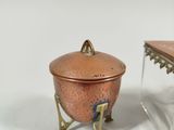 a small copper pot with a lid and a smaller copper pot with a lid