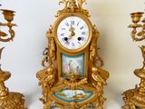 une horloge en or posée sur une table, à côté de trois bougies