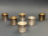 six coupes en argent ornées de motifs sur un fond gris