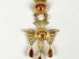 a close up of a gold pendant with a red stone on it