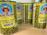 quatre boîtes de petits pois sont posées sur une table, avec une femme en arrière-plan
