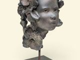 sculpture représentant la tête d'une femme posée sur un socle, avec une fleur dans les cheveux