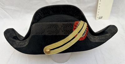 un chapeau de pirate noir orné de bordures dorées et rouges, posé sur une table blanche