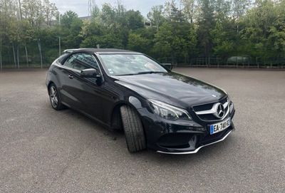une voiture noire garée sur un parking, avec des arbres en arrière-plan