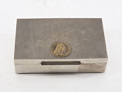 an antique silver cigarette case with a coin on top