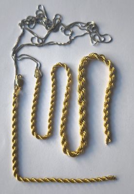 two gold chains and a silver chain on a white surface