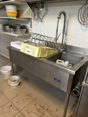 un évier en acier inoxydable dans une cuisine professionnelle, avec des casseroles et des poêles posées sur le plan de travail