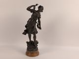 une statue antique en bronze représentant une femme tenant une fleur