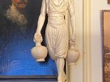 une statue représentant une femme tenant un vase devant un tableau