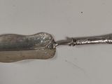une vieille cuillère en argent avec un manche en métal posée sur une surface blanche