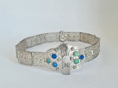 silver bracelet with blue and green stones on it on a white surface