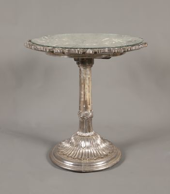 une table plaquée argent avec un plateau en verre sur fond gris