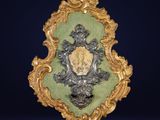 un cadre richement décoré, doré et vert, surmonté d'un blason