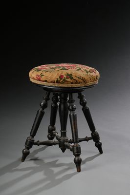 un tabouret ancien avec une assise rembourrée à motifs floraux et des pieds en bois