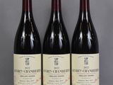 three bottles of wine sit on a glass table in front of a gray wall
