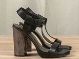 the heel of a woman ' s black high heeled sandals on a wooden table