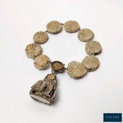 une image représentant un bracelet orné d'une clochette, posé sur une surface blanche